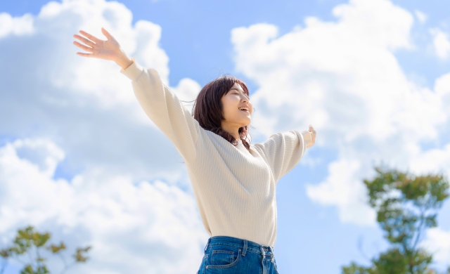 青空に両手を広げる笑顔の女性